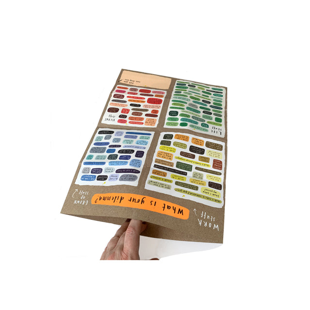 Hand holding open Mapology Guide showing colourful illustrated decision dilemmas