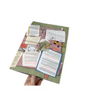 Hand holding open Mapology Guide Are You Looking for Answers showing illustrated table scene with books and notes