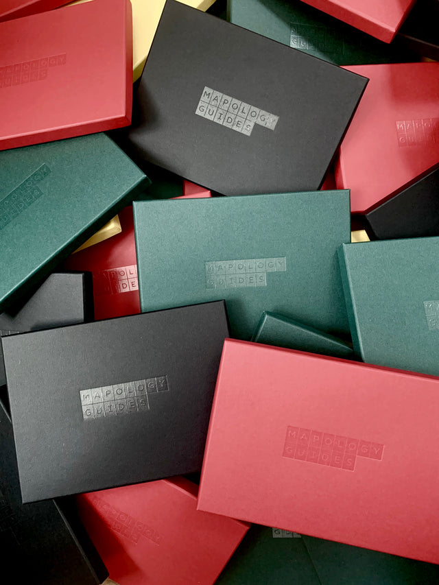 A pile of red, green and black gift boxes with the Mapology Guides logo printed on